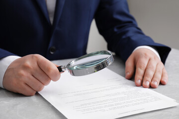 Man looking at document through magnifier at light grey table, closeup. Searching concept
