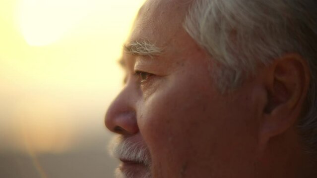 Close Up Asian Senior Man Face Practicing Meditation With Ocean Nature On The Beach At Summer Sunset. Retirement Elderly People Do Outdoor Relaxing Exercise. Mental Health Care And Motivation Concept.