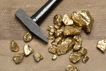 Pile of gold nuggets and hammer on wooden table, flat lay
