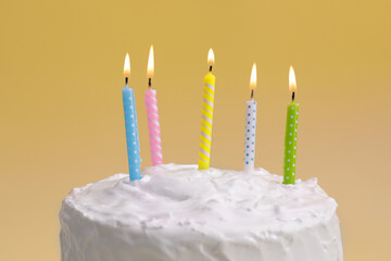 Delicious cake with cream and burning candles on yellow background, closeup