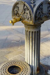 An iron fountain stands against the backdrop of a city. Its intricate detailing reflects the restrictions imposed by drought on a dry water source.