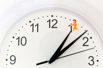 Biological clock: time pressure to have kids. Close up of clock with baby toy. Alarm for parenthood