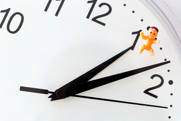 Biological clock: time pressure to have kids. Close up of clock with baby toy. Alarm for parenthood