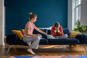 Loving supportive mother comforting upset crying teen daughter while sitting together on sofa at...