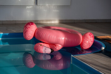 Inflatable pink flamingo upside down in swimming pool. After party hangover mood.