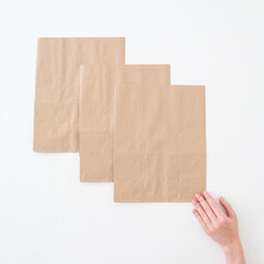 Fototapeta premium Craft bags on a white background with a hand. Place for text and logo. Top view. The concept of packaging, delivery, food.