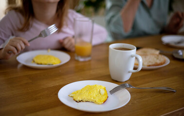 Side view of a family having breakfast in the kitchen with an omelette, a sandwich with butter and cheese, orange juice and coffee. Delicious and healthy breakfast. Selective focus on the coffee mug.