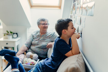 Obraz premium A school-age boy looks at photos taped to the wall, in a cozy room at home, side view