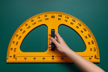 Woman holding protractor with measuring length and degrees markings near green board, closeup