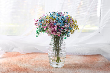 Beautiful gypsophila flowers in vase on textured table near window