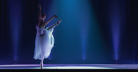 Cinematic Shot of Ballerina in Pointe Shoes and White Tutu Dancing and Rehearsing on Classic Theatre Stage with Dramatic Lighting. Graceful Classical Ballet Female Dancer Performing a Choreography © Kitreel