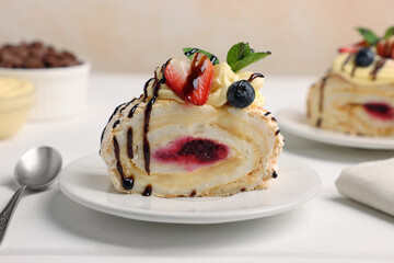 Piece of tasty meringue roll with jam, cream, strawberry, blueberry and mint on white wooden table, closeup