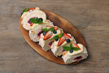 Pieces of tasty meringue roll with jam, cream, strawberry, blueberry and mint on wooden table, top view