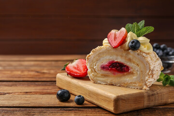 Piece of tasty meringue roll with jam, cream, strawberry, blueberry and mint on wooden table, closeup. Space for text