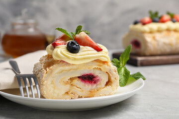 Piece of tasty meringue roll with jam, cream, strawberry, blueberry and mint on light grey table, closeup