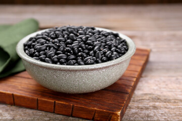Bowl of raw black beans on wooden table, closeup