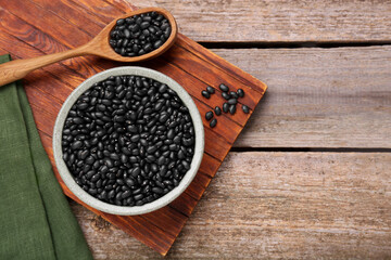 Bowl and spoon of raw black beans on wooden table, flat lay. Space for text
