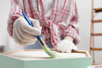 Woman painting honeycomb shaped shelf with brush indoors, closeup