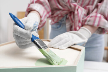 Fototapeta na wymiar Woman painting honeycomb shaped shelf with brush indoors, closeup