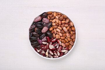 Bowl with different types of beans on white wooden table, top view