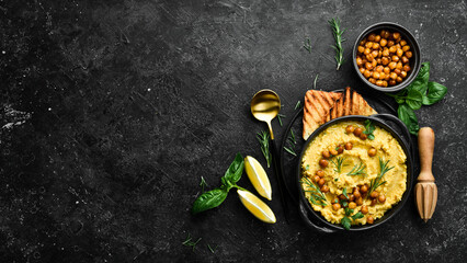 Hummus with chickpeas and rosemary in a black stone plate. Vegetarian food. Top view. On a black stone background.