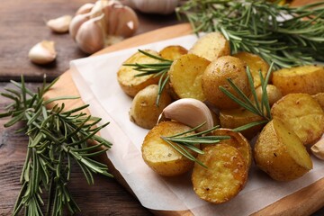 Fototapeta na wymiar Delicious baked potatoes with rosemary and garlic on parchment paper, closeup