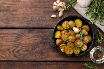 Delicious baked potatoes with rosemary and ingredients on wooden table, flat lay. Space for text