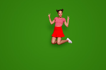 Full-length full-size view of jumping laughing and pretty woman dressed in colourful bright clothes shows a v-sign isolated on red background. Joy fun concept