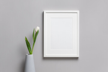 Blank vertical frame mockup with fresh tulip flower in vase, white mock up with copy space
