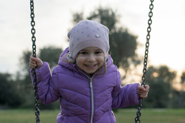 Ritratto di una bambina di tre anni molto allegra con giubbotto di colore viola e cappello.