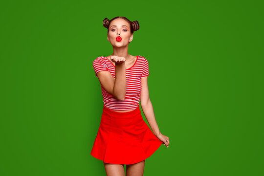 Cute girl send a kiss for you Adorable young girl with nice make up wearing striped tshirt and red skirt isolated on bright background and sends air kiss from open palm