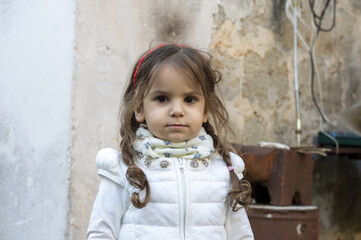 Ritratto di una bambina di tre anni molto allegra con gilet bianco e treccine.