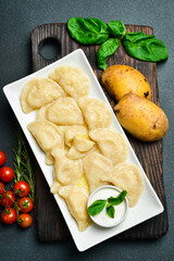 Ukrainian dumplings with potatoes and sour cream on a white square plate. Free space for text. On a dark background.
