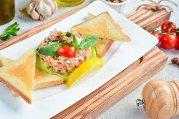 Tartar. Salmon, avocado and onion tartare with bread toast. On a white plate. On a gray stone background. Restaurant menu.