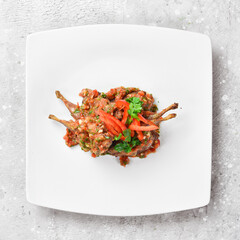 Quail baked in tomato sauce with vegetables. On a white plate. On a gray stone background....