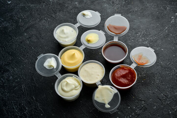 Obraz na płótnie Canvas Set of sauces. Ketchup, mayonnaise, tartar, chili, and mustard sauces in plastic containers. Takeaway food. On a black stone background. Rustic style.