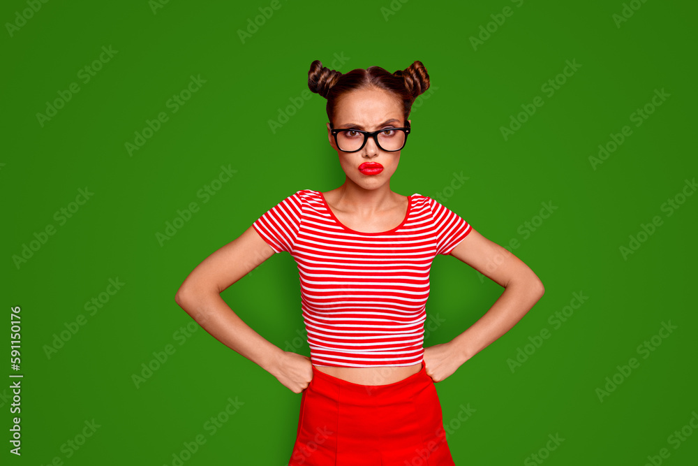 Wall mural Strict teacher Portrait of grimacing offended young gorgeous woman model with with hands on waist and bun hairstyle isolated on red background