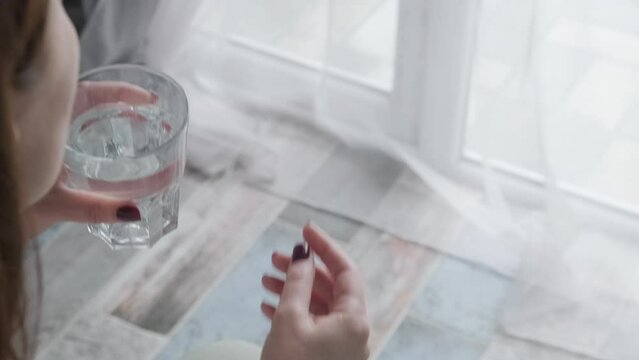 Woman taking white pill of statin medicine to treat high cholesterol or painkiller with glass of water at home. Taking medicine, health care, pharmacy and treatment concept. Selective focus