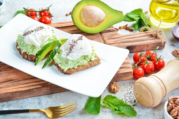 Fototapeta na wymiar breakfast Sandwich with poached egg and avocado. On a white plate. On a gray stone background. Restaurant menu.