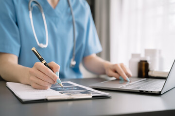 Doctor sitting at table and writing on a document report in hospital office. Medical healthcare staff and doctor service.