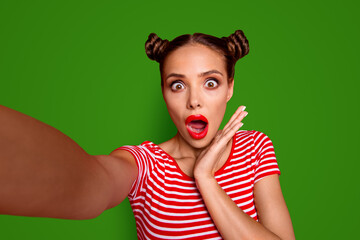 OOPS Self portrait of cute, trendy and shocked woman with bun hairdo wide open eyes mouth shooting selfie on front camera isolated on red background