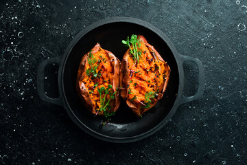 Vegetarian menu. Baked sweet potatoes with spices and garlic in a pan. Healthy food. On a black stone background.