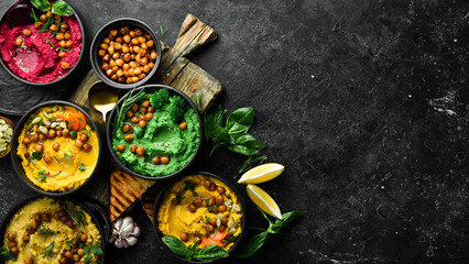 Colorful hummus bowls background. Different kinds of dips. Traditional hummus, herb hummus, beetroot hummus. On a concrete black background.