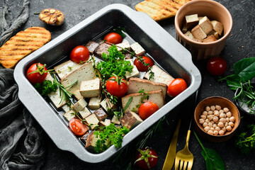 Tofu cheese. Salad of tofu cheese, tomatoes, olive oil and rosemary and spices in a bowl. On a stone background.