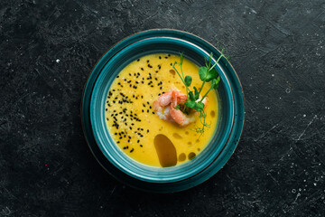 Autumn menu. Pumpkin soup with shrimp, olive oil and sesame seeds. In a blue bowl. On a black stone background.