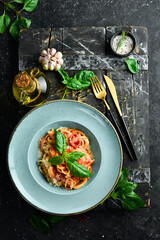 Pasta with chicken fillet, tomatoes and basil in a plate. Italian dish. On a black stone background.