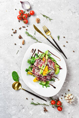 Salad: veal carpaccio, avocado, lettuce and orange. On a white plate. On a gray stone background. Restaurant menu.