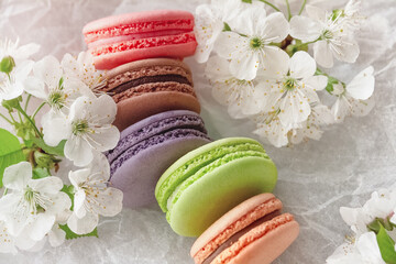 macaroons of red, brown purple, green and beige on white paper with apple blossoms