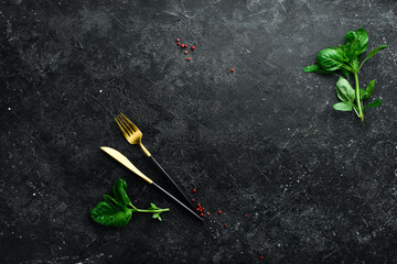 Cooking background: cutlery, spices and basil. On a black stone background. - obrazy, fototapety, plakaty