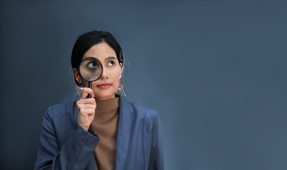 Businesswoman looking through magnifying glass on grey wall background. copy space